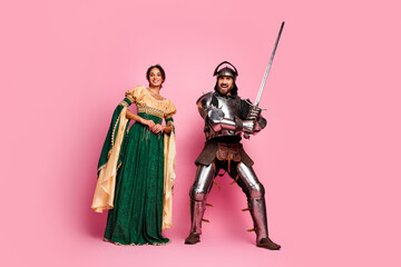 Couple in medieval costumes posing with pink background, blending elegance and courage