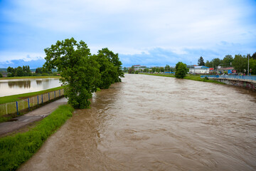 Overflowing river during flood with muddy water surrounded by trees and urban landscape under...