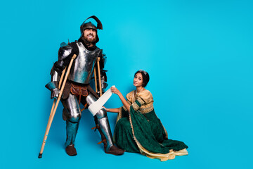 Themed costume portrait with a knight on crutches and a princess in an elegant gown against a pink...
