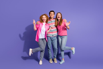 Fototapeta premium Group of cheerful young friends smiling and posing with joyful gestures against a vibrant purple backdrop
