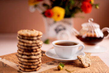 photo A cozy tea time experience with a warm cup of freshly brewed tea, a stack of delicious crispy cookies, and a beautiful floral arrangement adding charm to the setting.