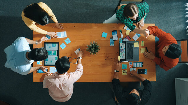 Programmer team brainstorm and plan Ux Ui design for mobile phone while present idea by using laptop at meeting. Software developer look at wireframe prototype while write at sticky note.Convocation.