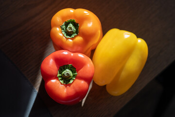 Fresh bell peppers in red, orange, and yellow hues sits on a wooden surface.