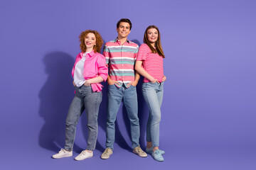 Fototapeta premium Group of three young friends standing together against a vibrant purple background, smiling confidently in casual outfits