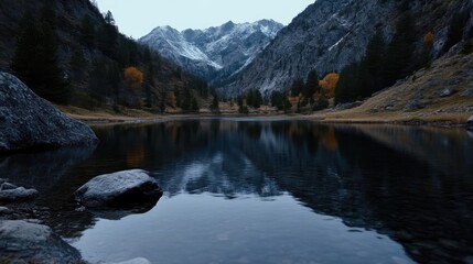 Serene alpine lake nestled in a valley, reflecting the surrounding mountains. Calm waters mirror the dramatic peaks, a tranquil scene. Autumn colors peak around the shore