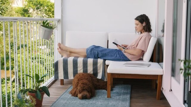 woman reading book on cozy balcony  relaxing summer routine, slow living aesthetic.
female enjoying quiet moment outdoors on sunny day, spending time with dog, mindful lifestyle scene