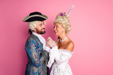 Elegant Couple in Historical Costumes Against Pink Backdrop Smiling