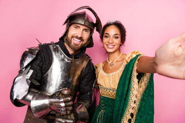 Medieval themed couple in elegant costumes posing against a pink backdrop, representing royalty and...