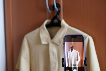 Smartphone photographing beige polo shirt hanging on hanger in closet