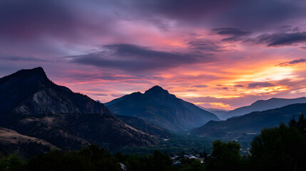A panoramic view of the sunset over the mountain range, with the sky painted in soft hues of pink, purple, and orange, and the peaks outlined in gold.