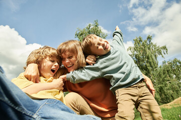 Low angle portrait of happy mother of two boys embracing and cuddling playfully outdoors against...