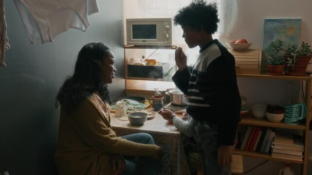 High angle shot of African American mother looking after her youngest child during breakfast, while her older child snacking
