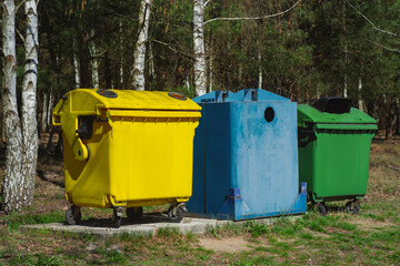 Three colorful recycling bins, yellow, blue, and green stand in forest. Eco-friendly waste sorting...