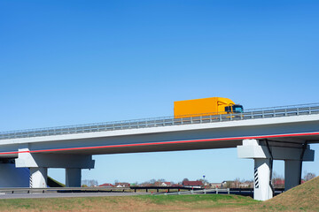 Fototapeta premium Mockup yellow truck travels on a highway overpass under a clear blue sky. Concept transportation and logistics.