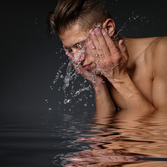 Young man washing his face in water on black background