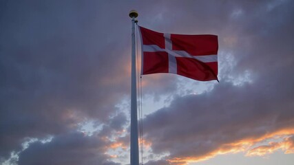 A vibrant and colorful Danish national flag is waving gracefully against a beautiful backdrop of a cloudy sunset sky