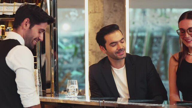 Smiling smart VIP customer inviting friend or couple for sitting at beverage counter bar talking with bartender while preparing welcome drink professionalism making great first impression. Vinosity.