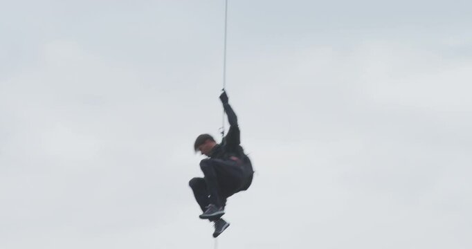 Man rappelling from helicopter with overcast sky - low shot