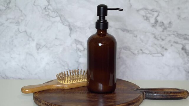 Amber glass shampoo bottle with bamboo hairbrush on dark wooden board and marble background. Minimalist natural, eco-friendly haircare and sustainable beauty product styling.