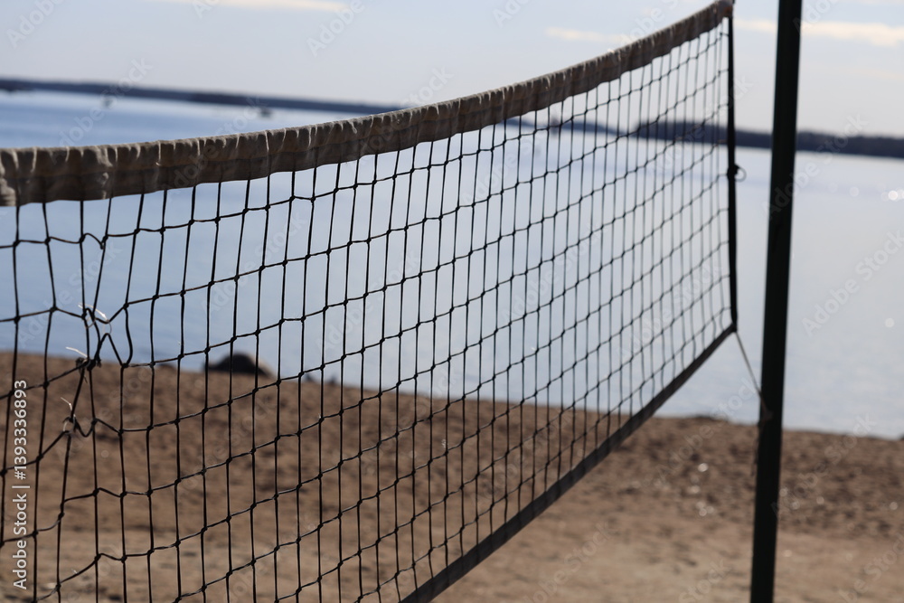 Poster a volleyball net on the beach near the water, perfect for a game or a relaxing day at the shore.