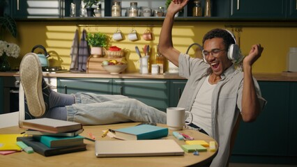 African American ethnic man happy carefree young male student gen z teen in headphones dancing moving at home kitchen studying relaxed guy music in earphones audio dance fun dance relax audio song