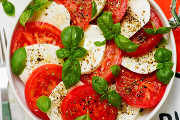 Traditional Italian caprese salad with tomatoes, mozzarella and basil on a white plate
