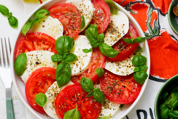 Traditional Italian caprese salad with tomatoes, mozzarella and basil on a white plate
