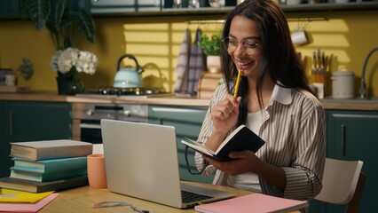 Latina woman smiling female girl student freelancer businesswoman working at home kitchen education distant studying class online teaching writing notes homework webinar video call laptop conference