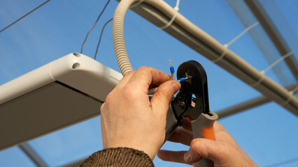 Installation of infrared heater in the greenhouse. Bringing the electrical cable. A man crimps the...