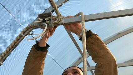 Electrical wiring in a polycarbonate greenhouse. A man brings the electric cable laid in corrugated...
