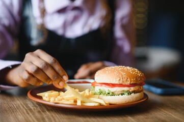 African girl eating burger and fries in cafe. Fast food concept