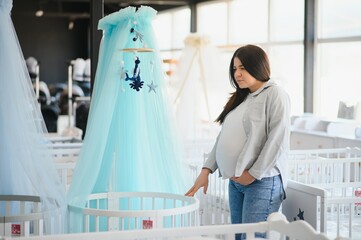 Happy pregnant woman choosing a baby crib in the store