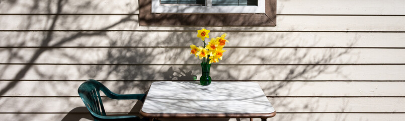 Folding table and plastic chair set up on wood deck to eat a meal outdoors at home, vase of...