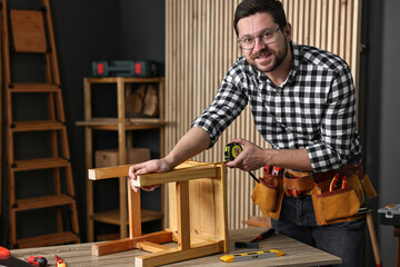 Repairman measuring wooden stool at table in workshop
