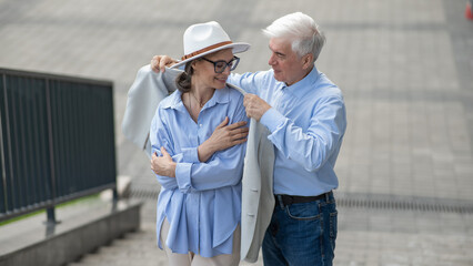 An elderly man puts his jacket on a woman. Romantic relationships of mature people. 