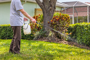 Man spraying weed killer herbicide on green grass residential yard. Landscaper using pump chemical...