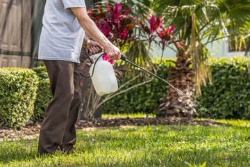 Man spraying weed killer herbicide on green grass residential yard. Landscaper using pump chemical pesticide sprayer for lawn weed control.