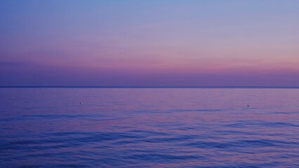 A sailboat glides across the calm waters at sunset