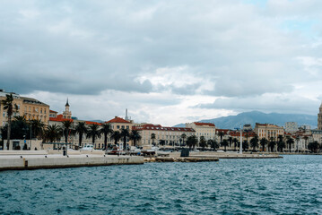 Naklejka premium Seafront promenade with historic buildings and palm trees under cloudy sky. Split, Croatia