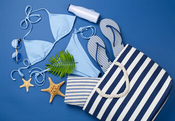 Blue beach bag with summer accessories on color background, top view
