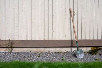 Spring gardening, shovel leaning against a light brown sided exterior house wall, sunny day to get...