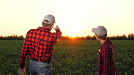 Man and woman agronomist colleagues discuss cultivation hitting hands at corn field closeup. Two farmer partners work as team consulting talking agriculture farming organic plant produce at sunset