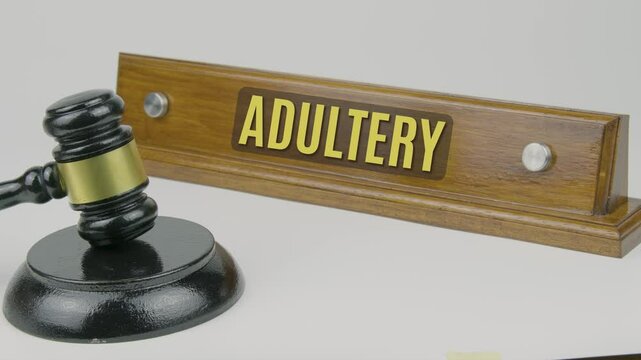 Adultery word on a wooden nameplate with a gavel tapping once and three times on a white background, representing marital infidelity, legal implications, and the violation of trust