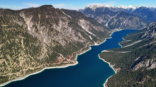 Aerial drone view of the beautiful Plansee Lake, located in the Austrian Alps. A view of crystal-clear waters, a sunny day and majestic mountains all around. 