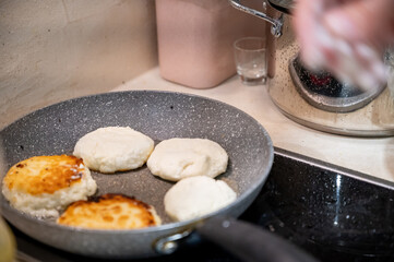 Frying Syrniki – Female Hands Covered in Dough and Flour. Close-up of female hands frying traditional syrniki (cottage cheese pancakes) in a frying pan.