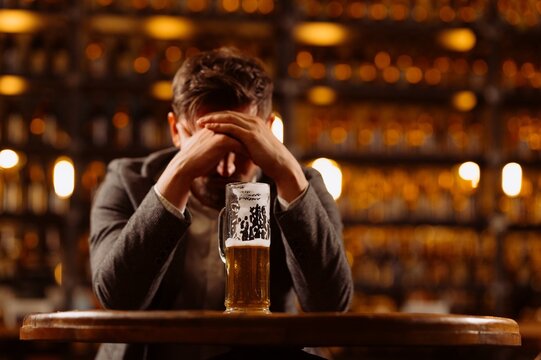 A man in despair sits at a bar with a glass of beer on the table