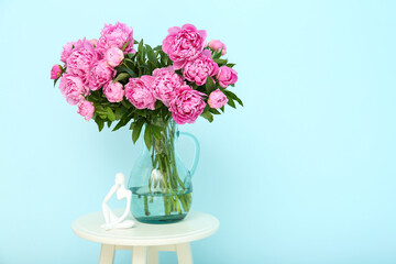 Vase of pink peonies with figurine on chair near blue wall