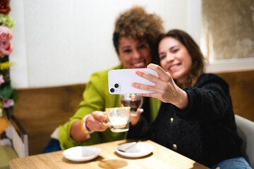 Two happy women taking selfie while drinking coffee at cafe