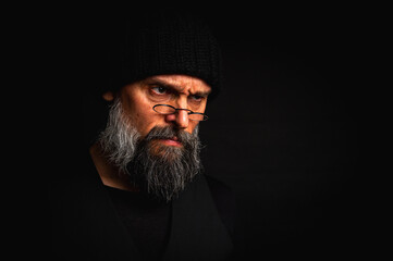 portrait, expressive mature man with a keen gaze and frown, wearing glasses and a knitted hat....