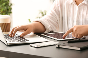 Female programmer working with laptop and tablet computer at her workplace in office, closeup